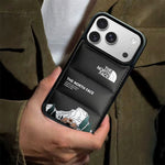 Black down-jacket style puffer iPhone case next to a speckled ceramic coffee mug on a dark table.